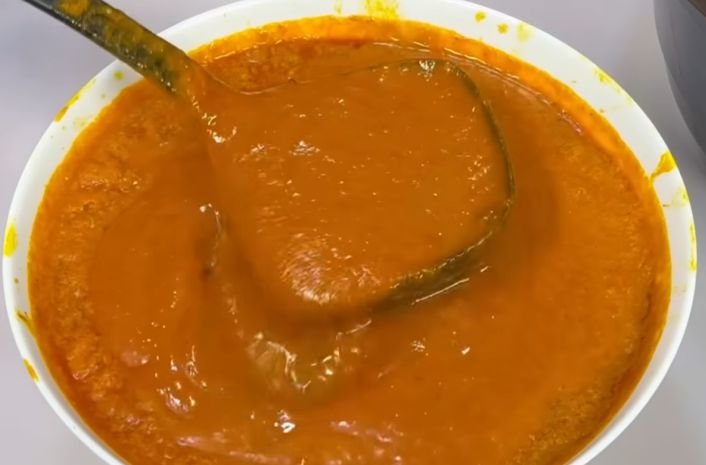 A fresh bowl of crude palm oil with a spoon scooping 